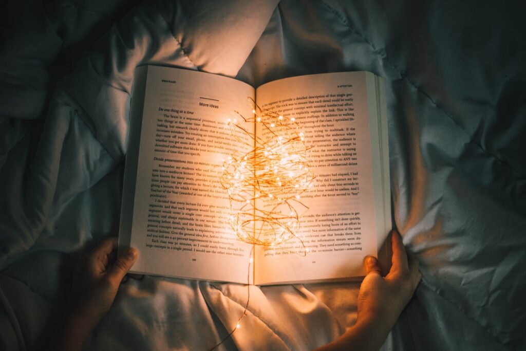 A book lies open on a bed with fairy lights spread across the open pages.